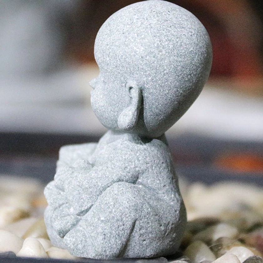 Rear view of monk holding book Buddha statue showing back detail on pebble stone surface