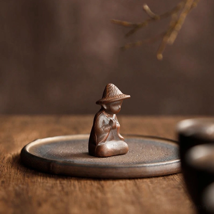 Front view of peaceful meditating monk ceramic incense holder figurine with matte glaze finish on wooden surface