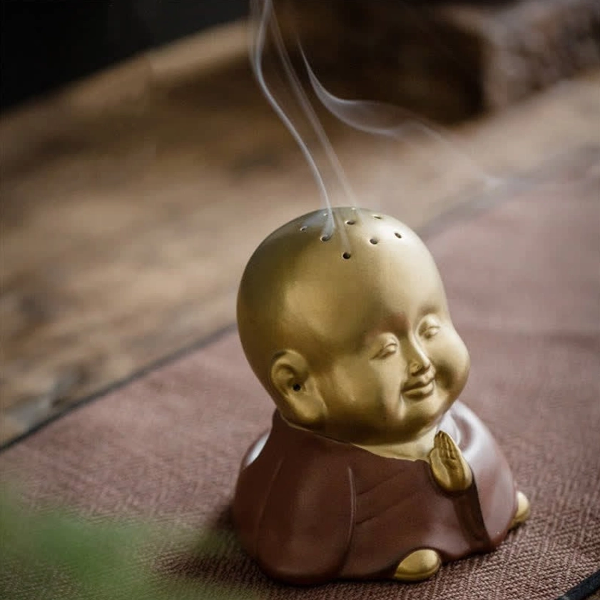 Monk incense burner side profile view on wooden tea table with woven mat, showing drifting incense smoke and dual-tone ceramic