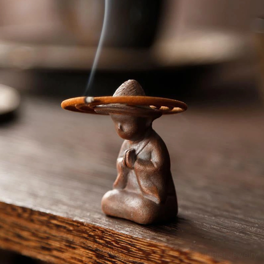 Low side angle close-up of textured brown ceramic monk incense burner with burning incense and rising smoke