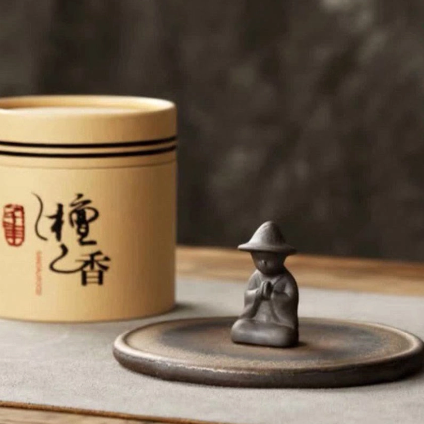 Monk ceramic incense holder displayed with sandalwood incense jar featuring Chinese calligraphy on minimalist tea table