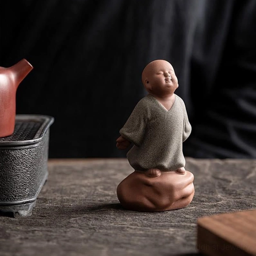 Grey ceramic monk figurine placed on tea table with traditional tea set, peaceful ambiance