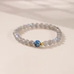 Moonstone lotus charm bracelet with gray moonstone beads, blue lotus charm, and gold accent beads displayed from angled top view