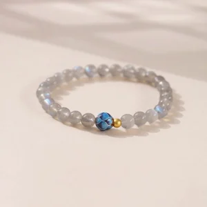 Moonstone lotus charm bracelet with gray moonstone beads, blue lotus charm, and gold accent beads displayed from angled top view