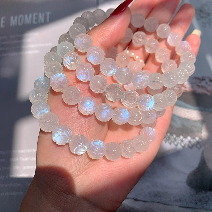 Hand-held moonstone lotus bracelet in palm, translucent beads with blue glow against natural daylight