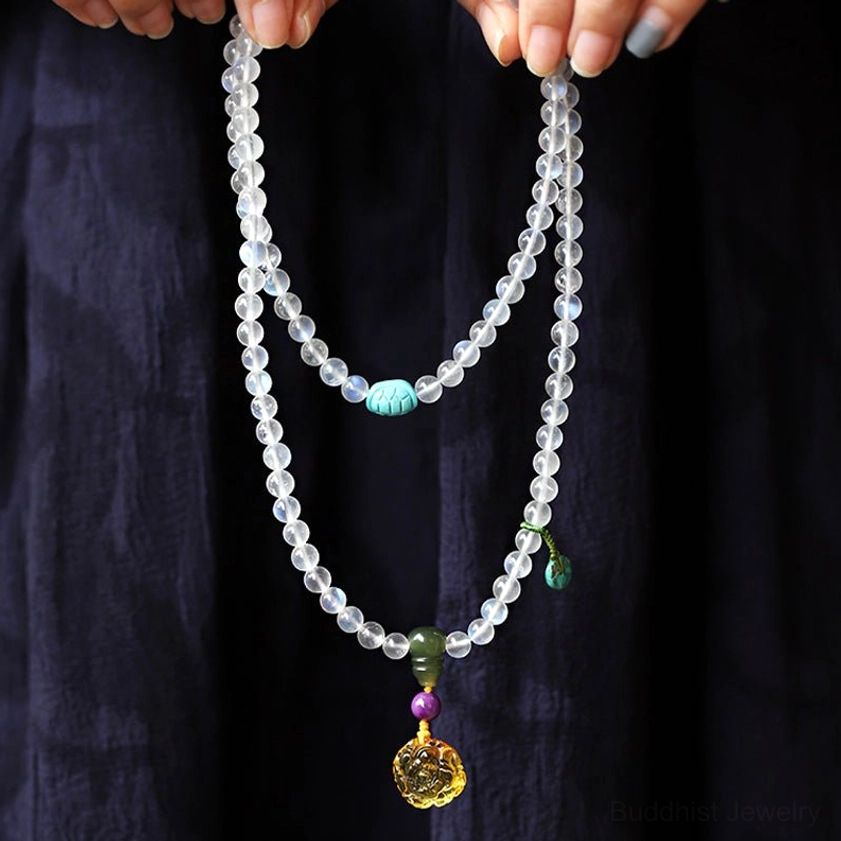 Moonstone mala necklace held in hands, translucent beads with lotus pendant on dark fabric background