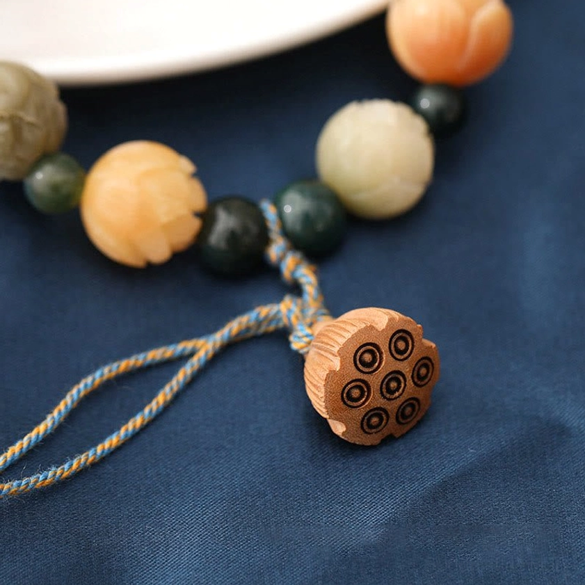 Overhead close-up of moss agate and stone beads with hand-carved wooden lotus pod showing intricate hole patterns