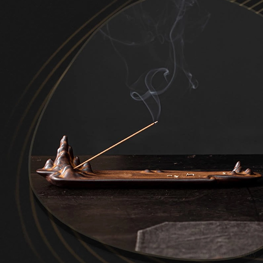 Mirror reflection view of ceramic mountain incense burner with curling incense smoke and brown retro matte finish on reflective surface