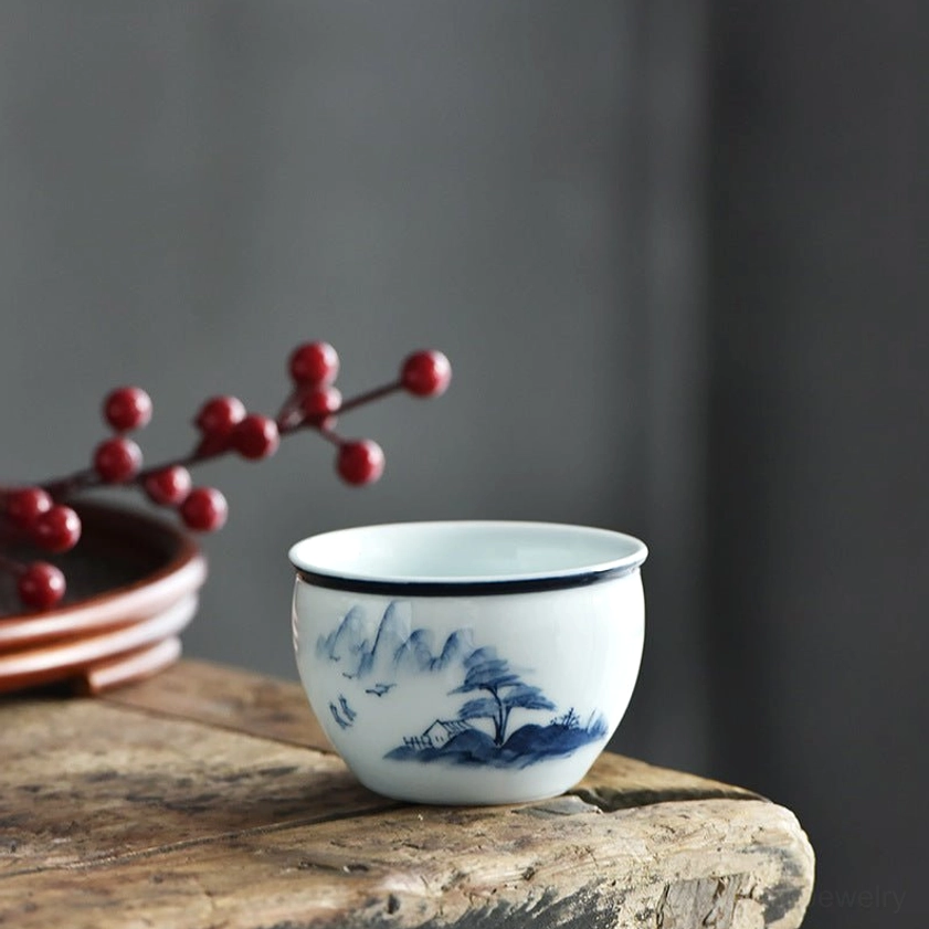 Blue and white ceramic teacup featuring pine trees and mountain peak landscape painting