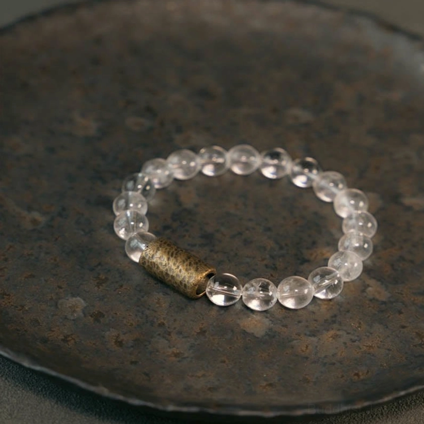 Multi-crystal protection bracelet with clear quartz and rutilated quartz beads on dark metal tray, flat lay overhead view