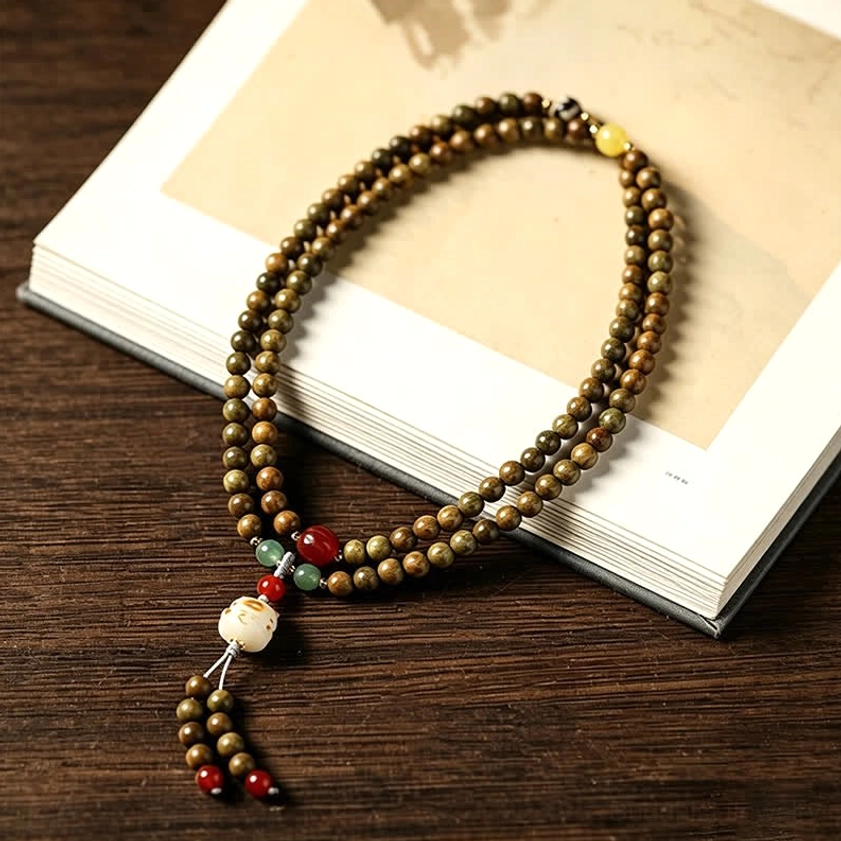 Multi-strand sandalwood mala necklace with red bead accent and tassel pendant on dark wood surface