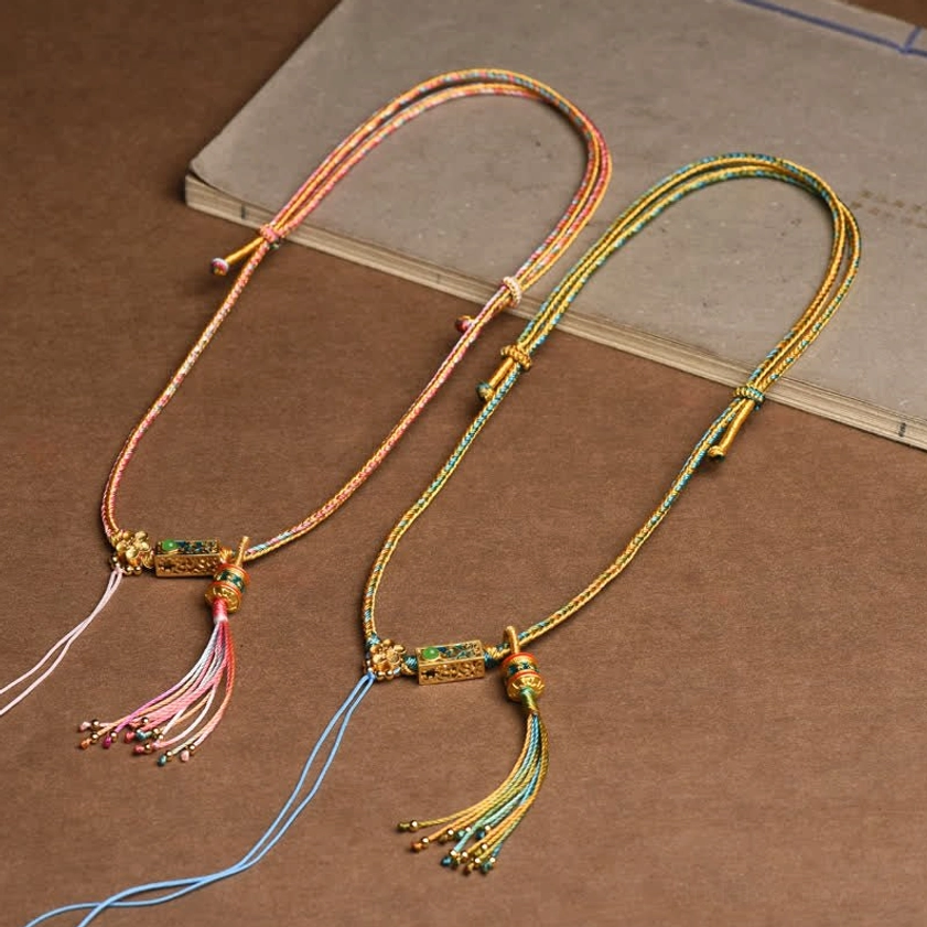 Two multicolor braided copper Buddhist necklaces displaying pink and blue color variations with enamel charms and decorative tassels