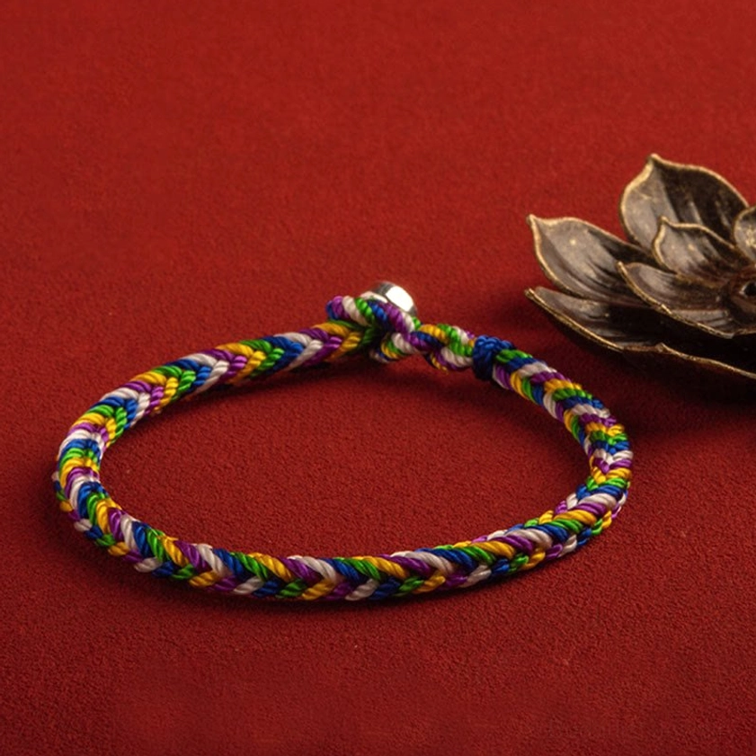 Multicolor Buddhist protection bracelet with silver metal clasp, overhead view on red background with bronze flower accent