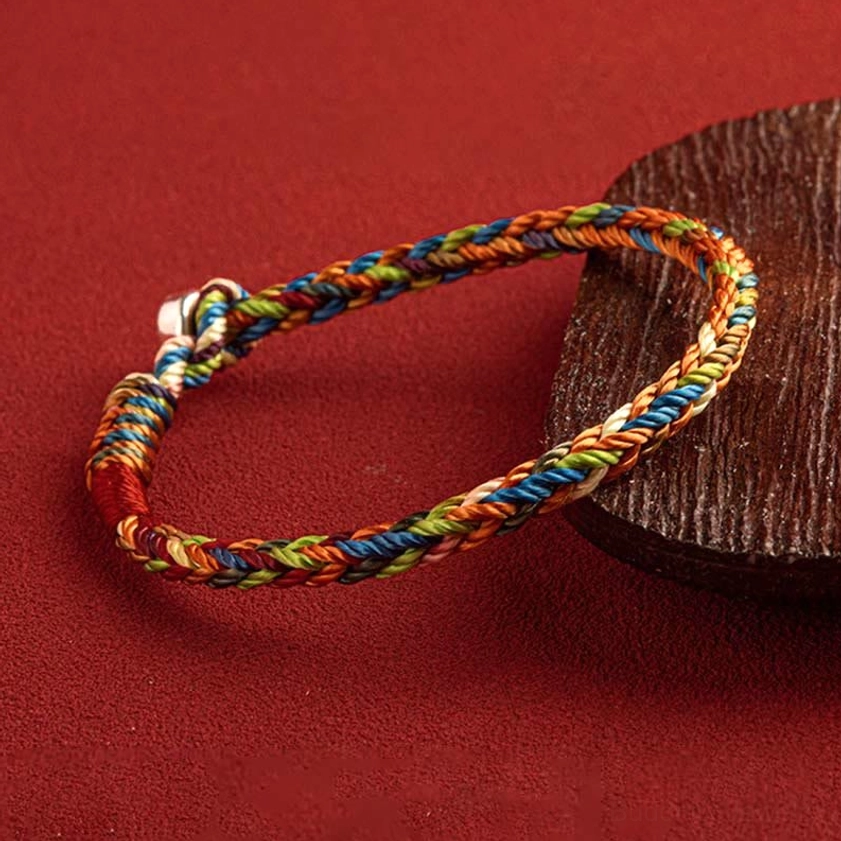 Side view of multicolor braided Buddhist bracelet with 925 silver clasp and red woven accent detail on fabric