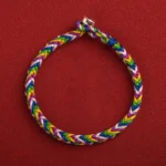 Multicolored five-color Buddhist lucky bracelet with silver clasp on red background, top-down flat lay showing braided rope and metal buckle