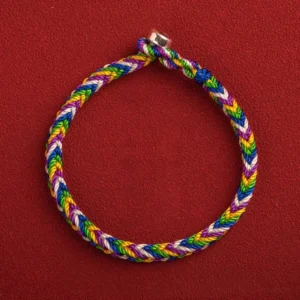 Multicolored five-color Buddhist lucky bracelet with silver clasp on red background, top-down flat lay showing braided rope and metal buckle
