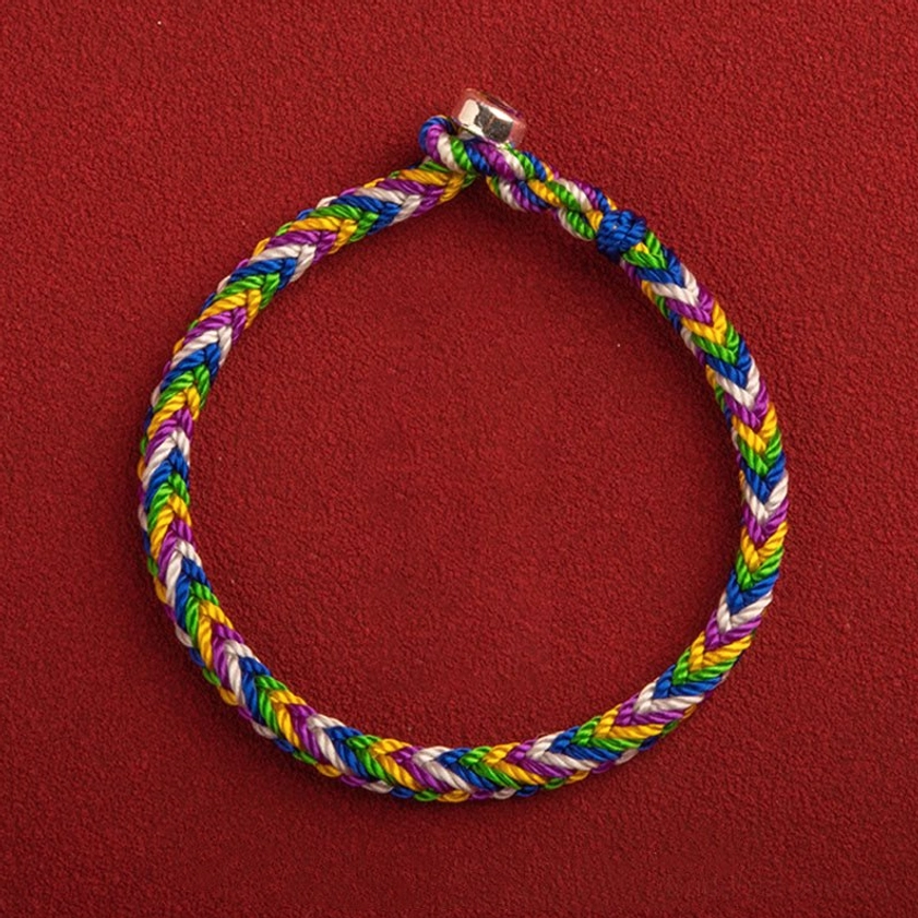 Multicolored five-color Buddhist lucky bracelet with silver clasp on red background, top-down flat lay showing braided rope and metal buckle
