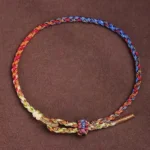 Handcrafted multicolor Buddhist string bracelet with red, blue, yellow and green threads, adjustable knot closure, flat lay on dark background
