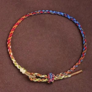 Handcrafted multicolor Buddhist string bracelet with red, blue, yellow and green threads, adjustable knot closure, flat lay on dark background