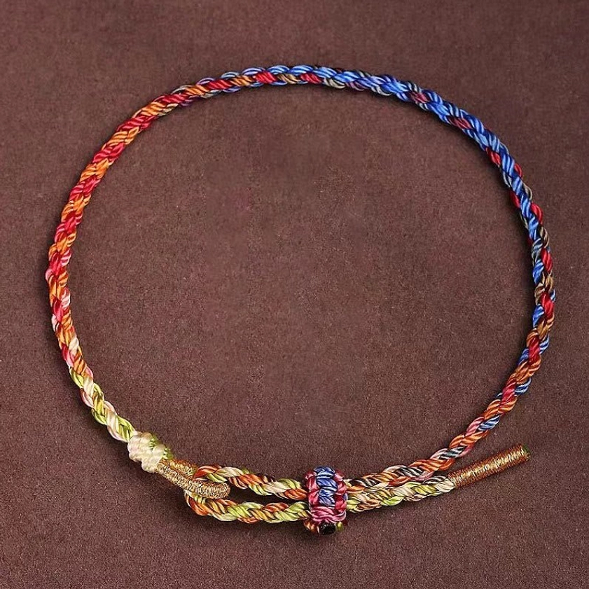 Handcrafted multicolor Buddhist string bracelet with red, blue, yellow and green threads, adjustable knot closure, flat lay on dark background