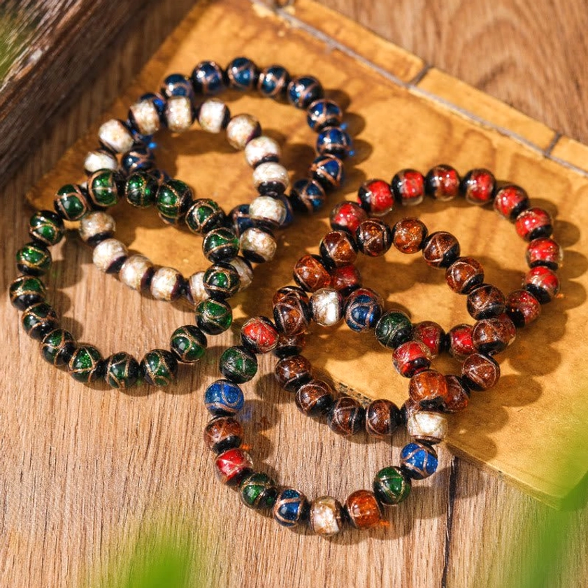 Collection of multicolor liuli glass Buddhist bracelets with metallic accents displayed on wooden surface with aged paper