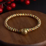 Handwoven multicolor lotus balance bracelet with copper charm bead on wooden coaster with red winterberry decoration