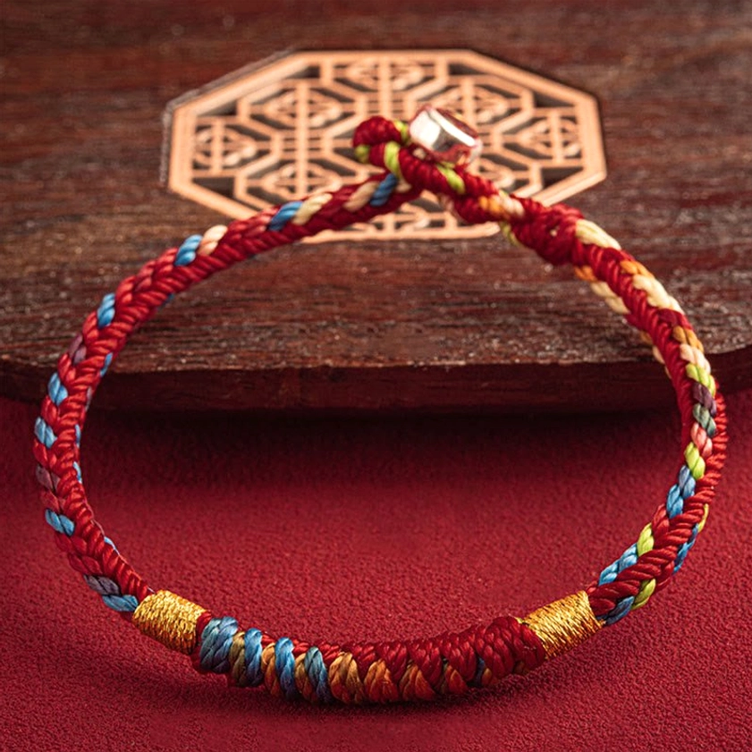 Complete multicolored Buddhist bracelet with King Kong Knot and silver buckle displayed on red backdrop with decorative wooden ornament