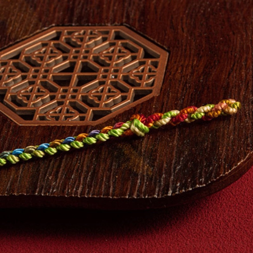 Multicolored braided Buddhist string bracelet sample strand showing gradient weave pattern on carved wooden tray
