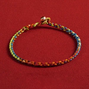 Multicolored Buddhist string bracelet with 925 silver clasp, handmade woven rainbow cord with metal bead detail, flat lay view on red background