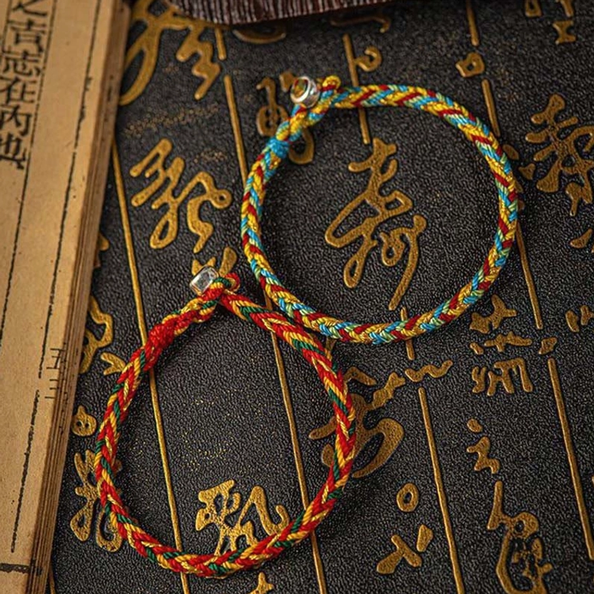 Side view of multicolored Buddhist protection bracelets showing red blue golden twisted threads and metal clasps against traditional Chinese longevity character