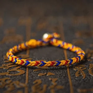 Handcrafted multicolored Buddhist string bracelet with silver clasp and King Kong knot, featuring red orange green and blue woven threads on dark background with sacred symbols