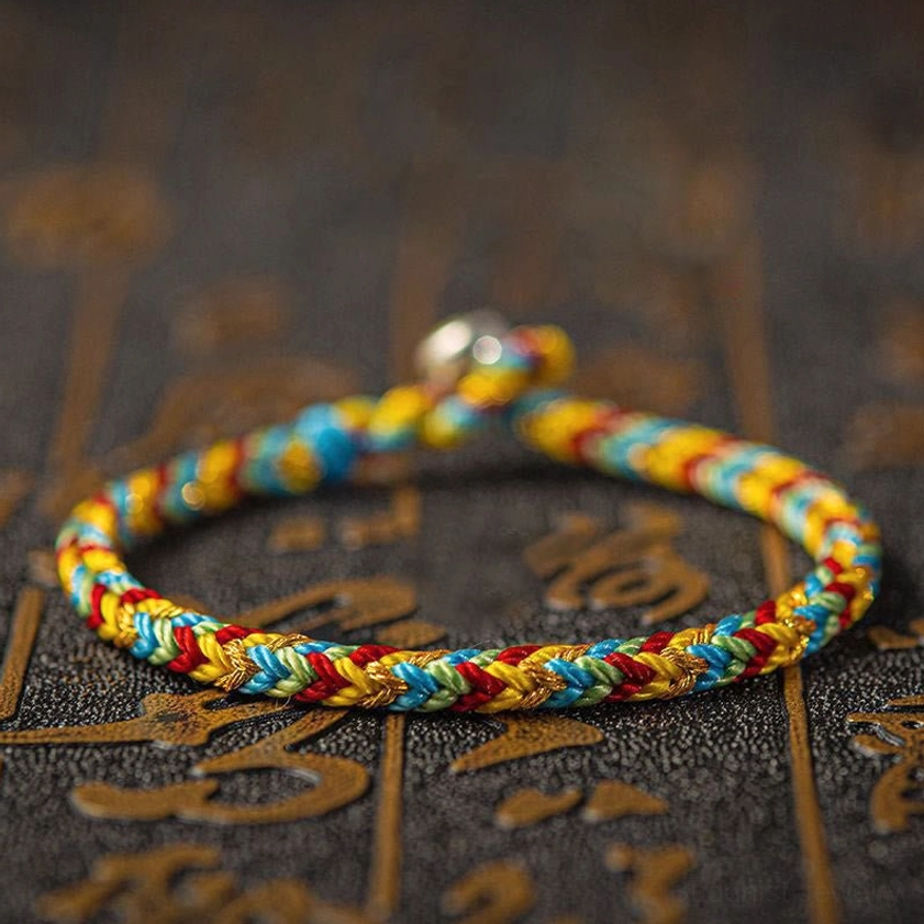 Single handmade multicolored Buddhist bracelet with smooth twisted braid design, featuring orange red green and blue woven threads with metal clasp