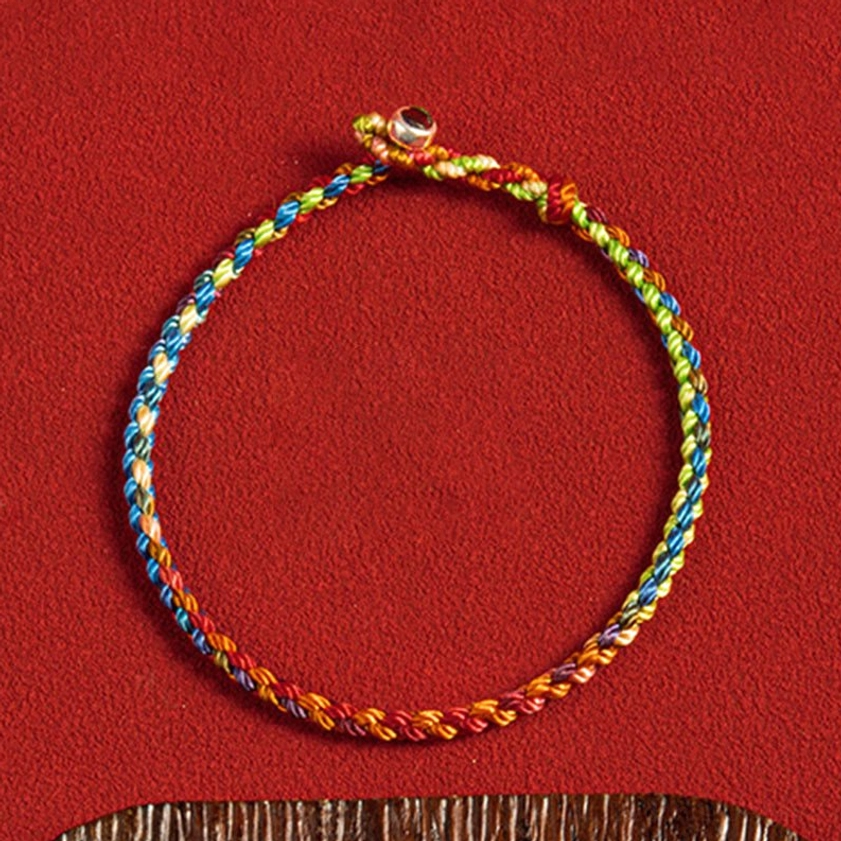 Handwoven multicolored Buddhist string bracelet with metal bead clasp and twisted colorful rope on wooden base