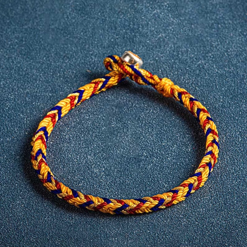 Top-down close shot of handwoven multicolored Buddhist protection bracelet with red, yellow and blue woven threads and metal toggle charm