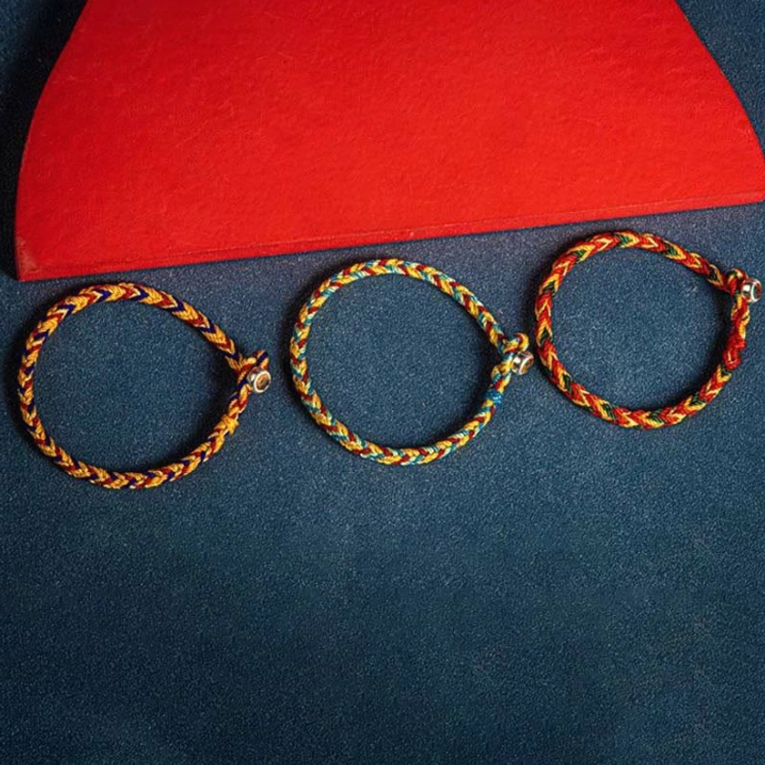 Three neatly arranged handwoven multicolored Buddhist bracelets showing consistent braided pattern and silver charms on colorful background