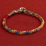Multicolored Buddhist string bracelet with King Kong knot weave and metal clasp, front top view on dark red background