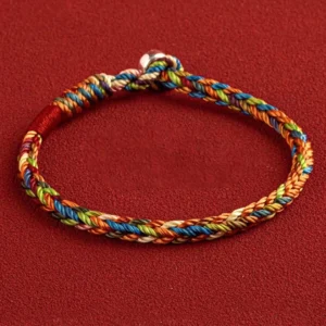 Multicolored Buddhist string bracelet with King Kong knot weave and metal clasp, front top view on dark red background