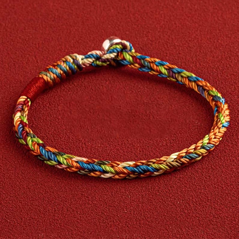 Multicolored Buddhist string bracelet with King Kong knot weave and metal clasp, front top view on dark red background