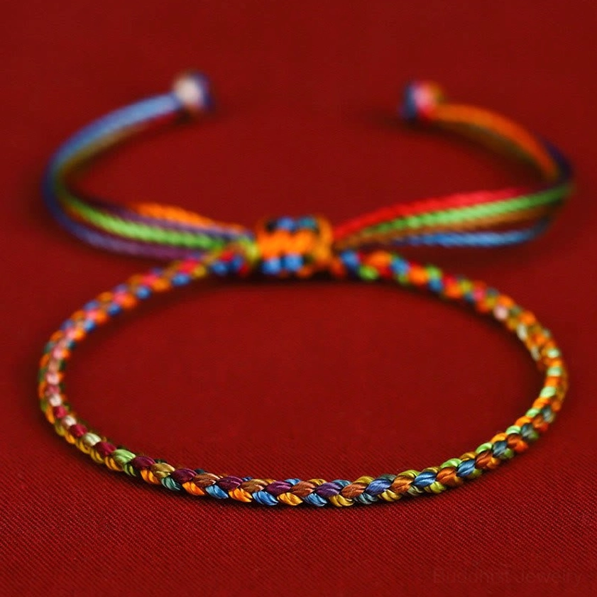 Multicolored Buddhist string bracelet with handwoven rainbow braid and adjustable pull-tie knot on dark red background