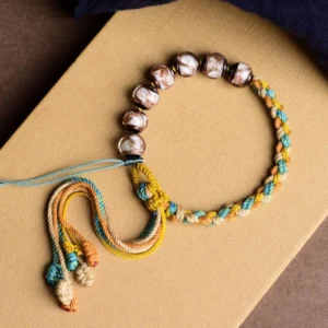Handmade multicolored Liuli glass bead braided bracelet with decorative knotted tassel on kraft paper background