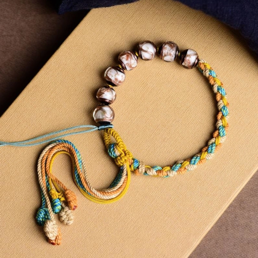 Handmade multicolored Liuli glass bead braided bracelet with decorative knotted tassel on kraft paper background