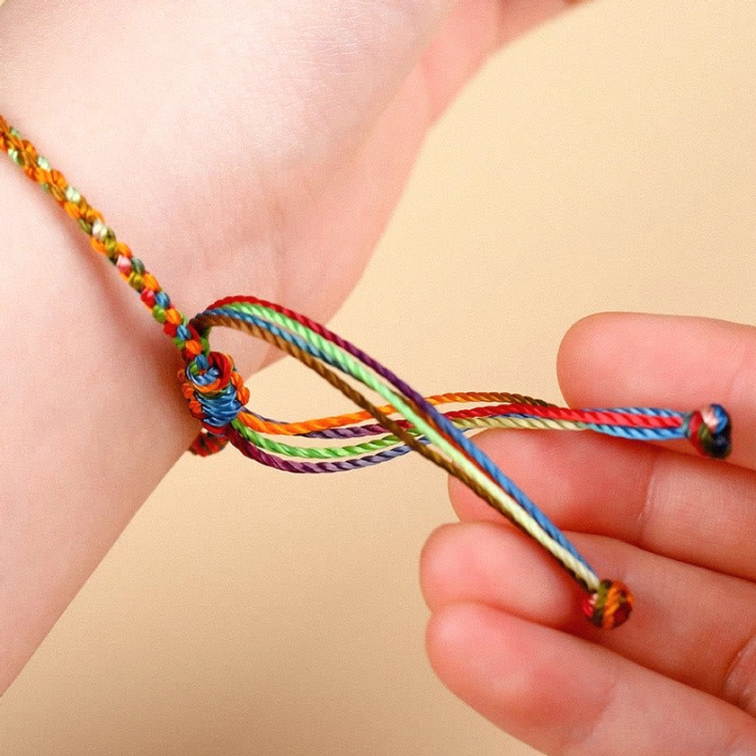 Closeup of multicolored Buddhist protection bracelet worn on wrist showing intricate silk braid texture and adjustable knot