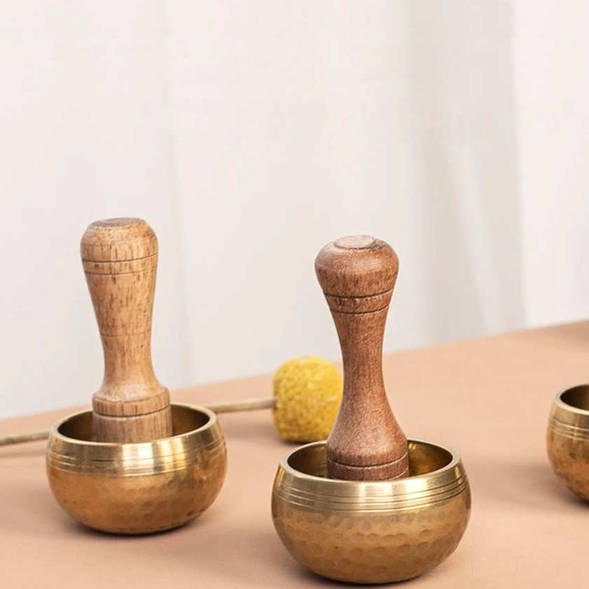Multiple handmade singing bowls with wooden mallets displayed on decorative table for group meditation