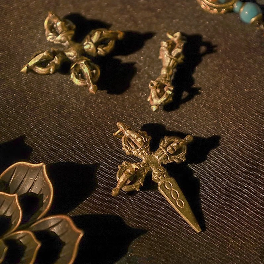 Multiple handmade brass dorje ornaments with varying vajra styles on brown fabric background, showcasing different Buddhist vajra designs with vintage metal finish