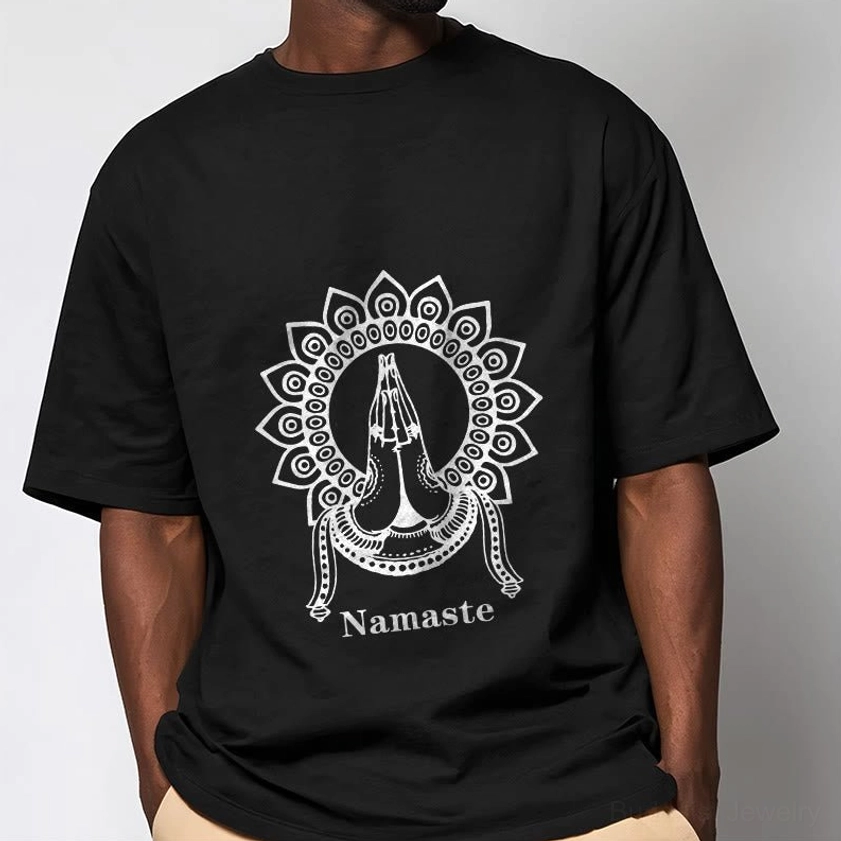 Male model wearing black Namaste mandala Buddhist t-shirt with white prayer hands graphic on light gray studio background