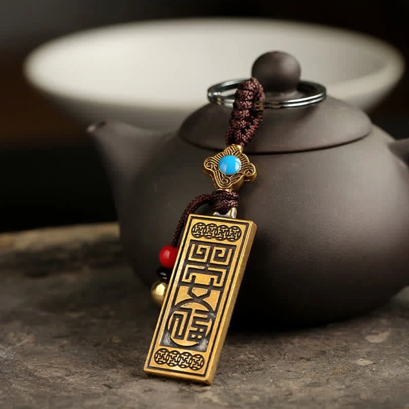 Three-quarter front view of Buddhist blessing keychain with blue enamel ornament and red beads on clay pot background