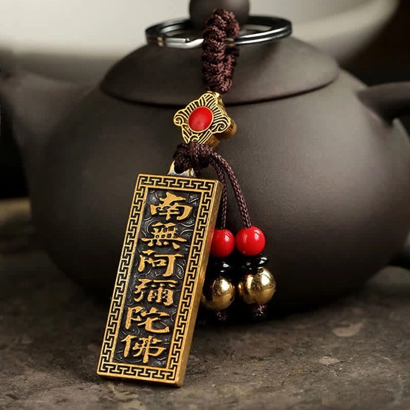 Namo Amitabha Buddhist blessing keychain with bronze sutra tag and red beads placed beside dark clay teapot
