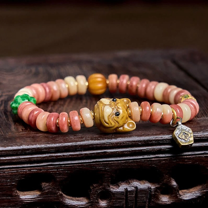 Handcrafted camel bone pug charm bracelet with gradient pink beads, amber accent, green stone, and carved charm on dark wooden base