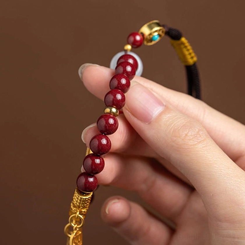 Natural cinnabar ruyi car hanging ornament featuring maroon stone beads, gold filigree, and traditional Buddhist blessing symbols for spiritual protection