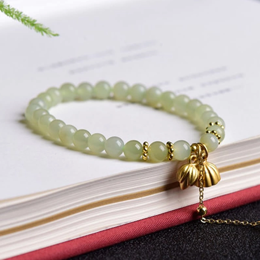 Hetian jade lotus bracelet on red-edged book, flat lay top-down view showing uniform pale green beads